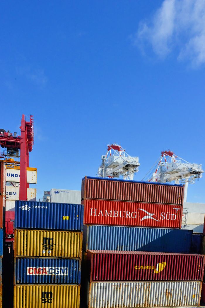 services-01 Colorful cargo containers stacked at a busy shipping port under a clear blue sky.